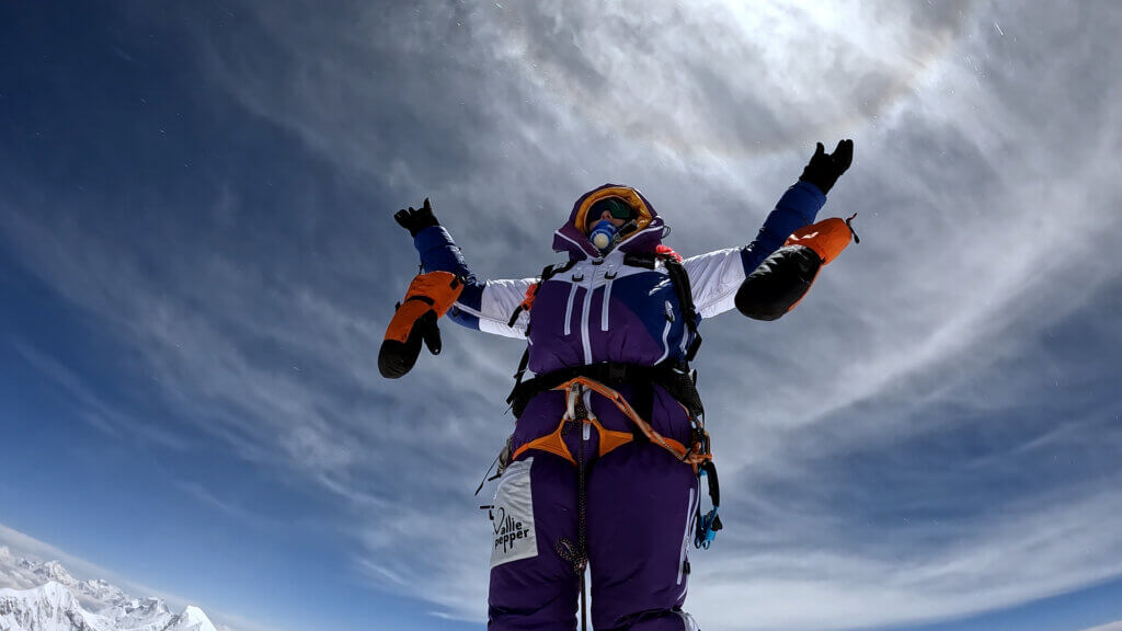 Allie Pepper standing on a snowy summit with arms raised